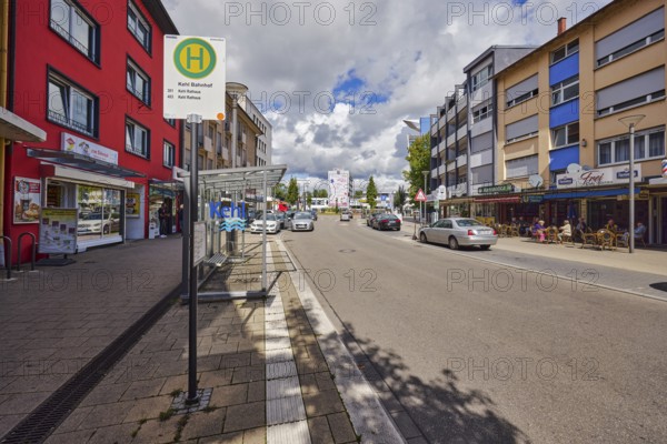 Bus stop Kehl station, bus shelters, general architecture, houses, row of houses, residential buildings and commercial buildings, shops, retail, parking strips with vehicles, outdoor area of a restaurant, bistro, café, pub, blue sky, cumulus clouds, main street, Kehl, Upper Rhine Plain, Ortenau district, Baden-Württemberg, Germany
