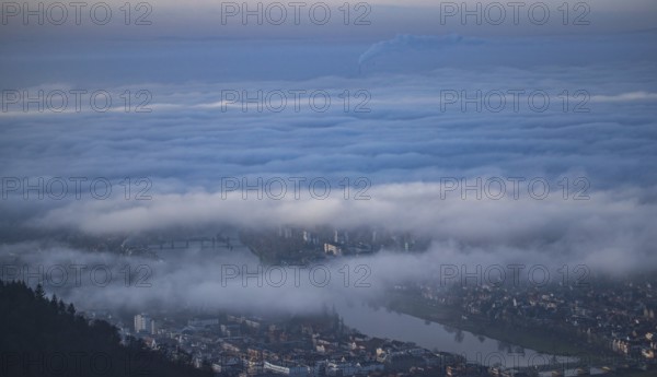 Aerial view of the city of Heidelberg on the Neckar, sea of fog from low-hanging clouds and fog fields, sunlit above the roofs of the city and the Neckar river, floating and waving with large and smoking chimney vents sticking out of the fog in the background, Heidelberg, Baden-Württemberg, Germany