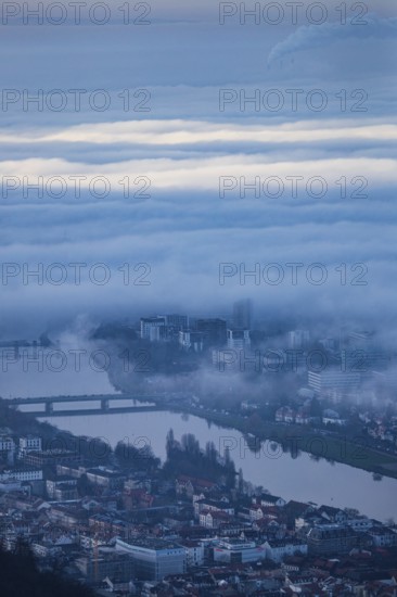 Aerial view of the city of Heidelberg on the Neckar, sea of fog from low-hanging clouds and fog fields, sunlit above the roofs of the city and the Neckar river, floating and waving with large and smoking chimney vents sticking out of the fog in the background, Heidelberg, Baden-Württemberg, Germany