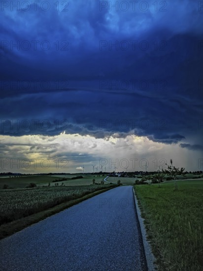 Supercell, approaching thunderstorm with impressive and threatening cloud formation, a thunderstorm over a country road and a village with wind turbines in the background, Baden-Württemberg, Germany