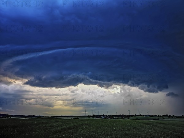 Supercell, approaching thunderstorm with impressive and threatening cloud formation of a thunderstorm over a village with wind turbines in the background, Baden-Württemberg, Germany