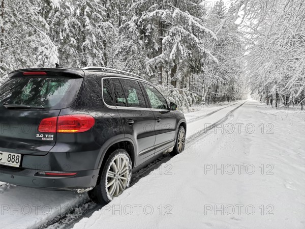 SUV driving in lane across heavily snow-covered road with lots of snow through a winter forest, Baden-Württemberg, Germany
