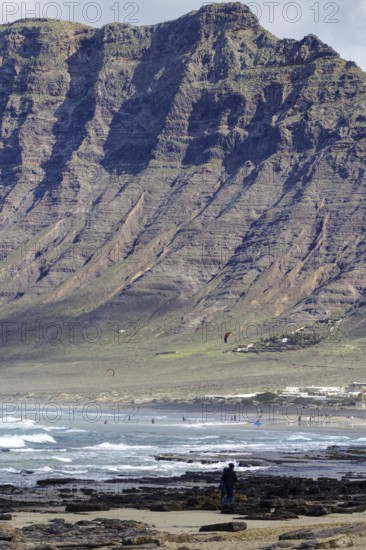 Beach with rocks and cliffs (Risco de Famara) in the background, people enjoying the sea, Caleta de Famara, Teguise Lanzarote