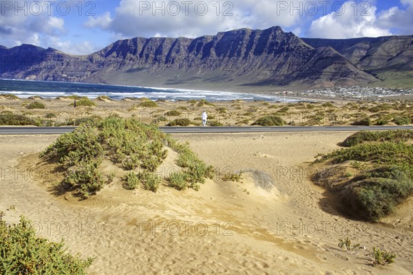 Beach with dunes and vegetation in front of a mountain range and cloudy sky, Caleta de Famara, Teguise Lanzarote