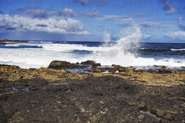 Dramatic scene of waves hitting black rocks on a sunny day, Playa de Caleta de Famara, Teguise Lanzarote