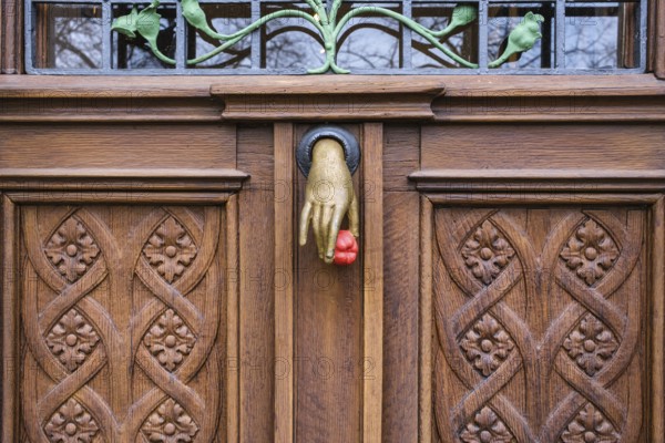 A cast iron door knocker on a wooden, artfully decorated front door in the shape of a hand holding a fruit, art nouveau, bushel castle, Mettnau peninsula, Radolfzell am Lake Constance, district of Constance, Baden-Württemberg, Germany
