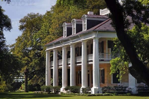 Classic southern house with columns and an extensive veranda surrounded by lush greenery, zero