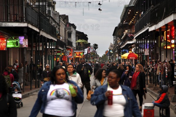 Lively nighttime scene on Bourbon Street with numerous passers-by and illuminated shops, New Orleans, Louisiana, USA