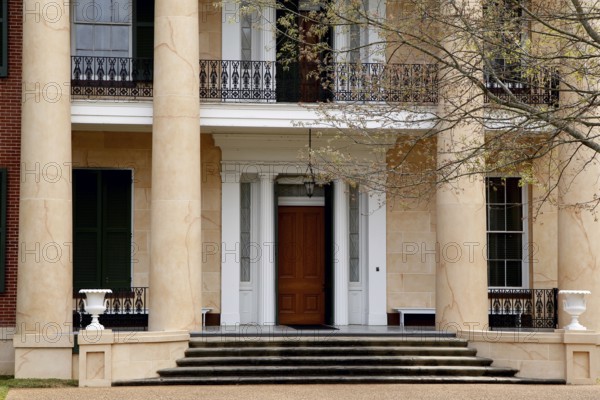 Entrance of an elegant house with large pillars and wooden door, surrounded by trees, Natchez, Mississippi, USA