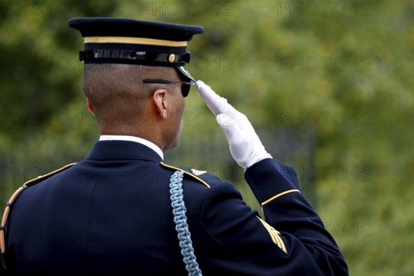 A soldier in formal uniform salutes during a formal ceremony, tree belt in the background, Washington D.C, USA