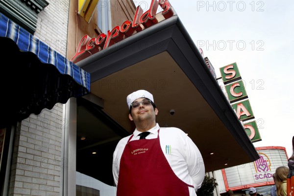 Ice cream parlour worker in uniform poses smiling in front of Leopold's ice cream parlour with retro animated signs, Savannah, Georgia, USA