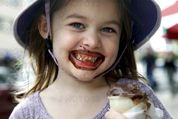 Happy girl with chocolate ice cream on her face smiles at the camera. Wears a summer hat, Savannah, Georgia, USA