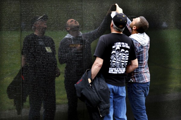 Men look at and touch the engravings of the wall of the Vietnam Veterans Memorial in a thoughtful gesture, Washington D.C, USA