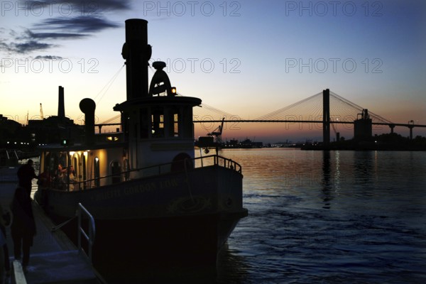 Silhouette of a ship on the Savannah River at sunset. A bridge can be seen in the background, Savannah, Georgia, USA