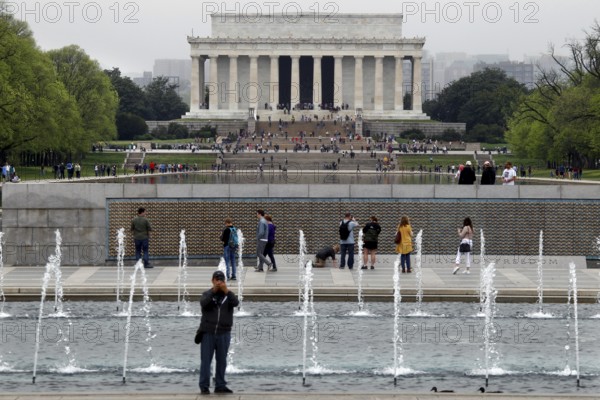 Visitors in front of a fountain looking at a historic monument in the distance, Washington D.C, USA