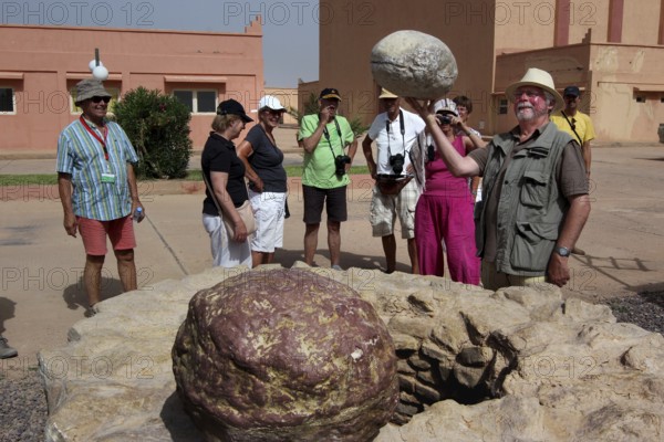 Group of tourists taking a guided tour of the CLA Studios in front of a big rock, Ouarzazate, Morocco