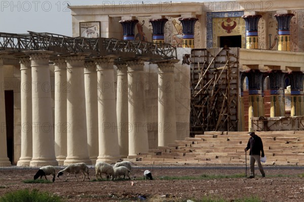 Film set with ancient columns and decoratively decorated building, a human leading goats past, Ouarzazate, Atlas Film Studios, Morocco