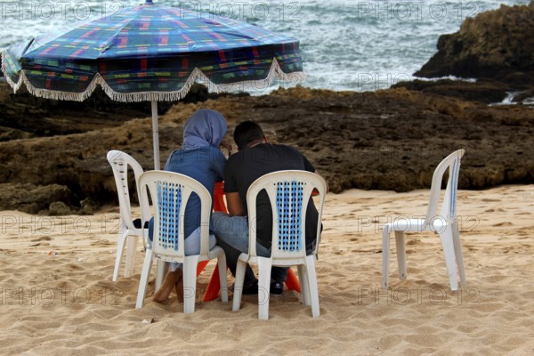 Two people sitting under a colorful sunshade on the beach in Oulidia, Oulidia, Morocco