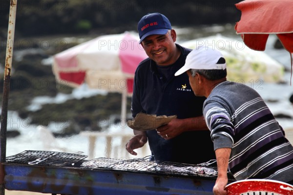 Two men talking at a food stall on the shore with a view of the sea, Oulidia, Doukkala-Abda, Morocco
