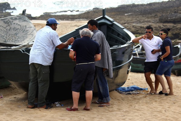 Group of people gather around a fishing boat on the beach in Oulidia, Oulidia, Doukkala-Abda, Morocco