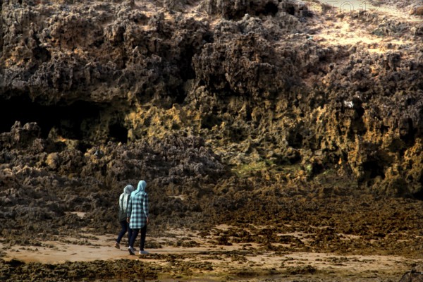 Person walking along rocky stretches of beach in Oulidia, Morocco, Oulidia, Doukkala-Abda, Morocco
