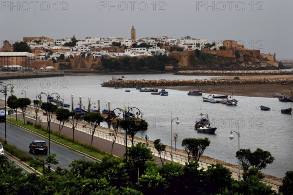 View across the river to the historic town of Salé with boats and city wall under cloudy sky, Rabat, Salé, Morocco