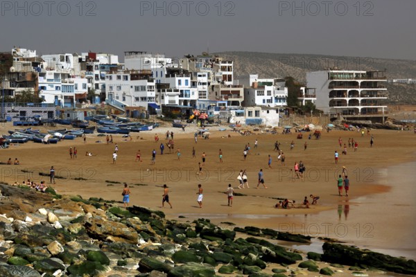 Busy beach with fishing boats and white buildings on the shore, Taghazout, Souss-Massa region, Morocco