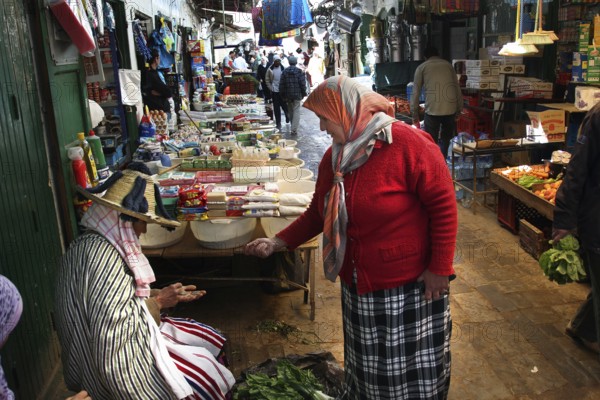Two woman in traditional clothing talking at a busy market, Tetouan, Medina, Morocco