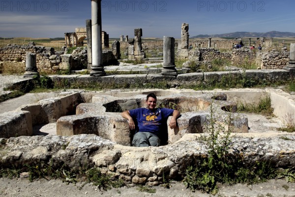 Visitors relax in the ruins of the Volubilis thermal baths, surrounded by ancient columns and stone structures, Volubilis, Morocco, Morocco