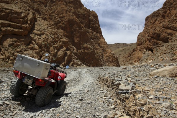 A quad bike rides through a rocky gorge under a clear sky, Tal, Tizgui n'Ouadda