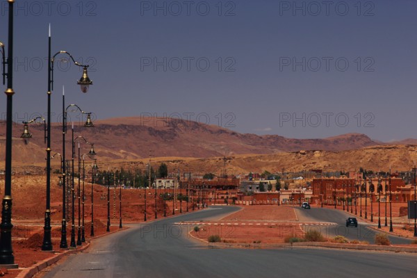 Curvy road with lanterns in sandy surroundings and hills in the background, Tinerhir, Morocco