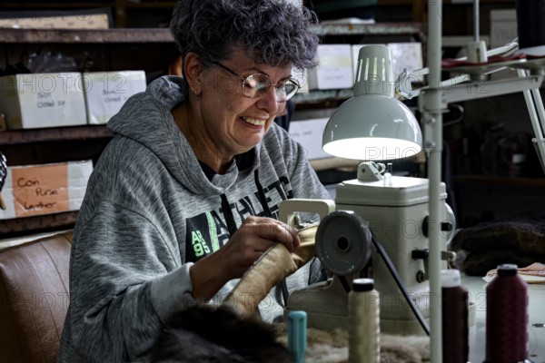 Seamstress works concentrated with thread and material under a lamp in a Possum factory, Stratford, New Zealand