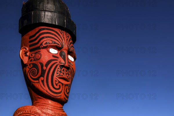 Large carved Maori figure painted red against deep blue sky in Whakarewarewa village, Rotorua, North Island, New Zealand