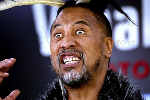 Maori man with aggressive facial expressions and feather headdress at a performance, Rotorua, Bay of Plenty, New Zealand