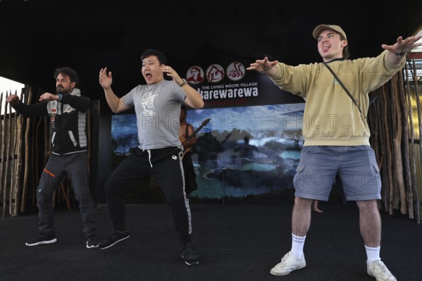 Three tourists taking part in a Haka performance and having fun on stage, Rotorua, Bay of Plenty, New Zealand