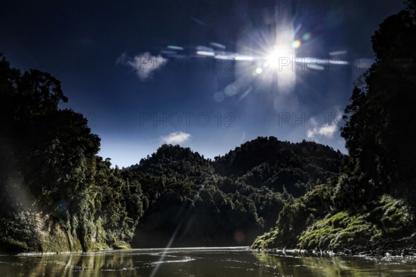 The sun shines over the wooded hills of the Whanganui River and meets calm water, zero