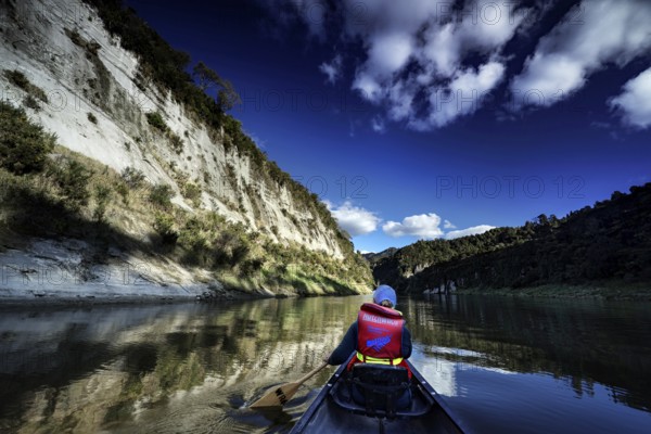 Paddler on calm river between high cliffs under bright blue sky near Whanganui River, zero
