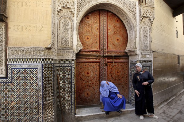 Two men in front of an artfully decorated wooden door with mosaic decoration, Fez, Fez el Bali, Morocco