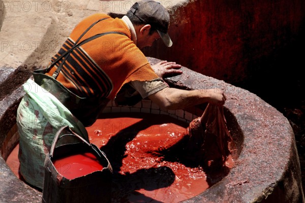 A worker dyes leather in a bright red basin in the tannery of Fez, Fez, el-Bali, Chouwara, Morocco