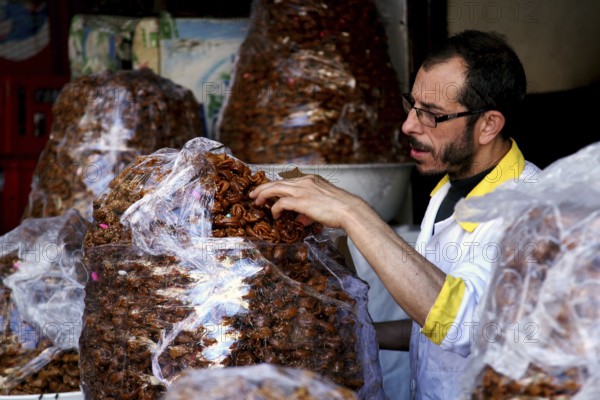 Merchant packs dates from large bags in a candy store, Fez, Fez el Bali, Morocco