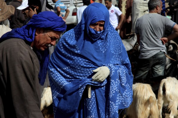 Man and woman in blue robes at a cattle market with goats, Guelmim, Morocco