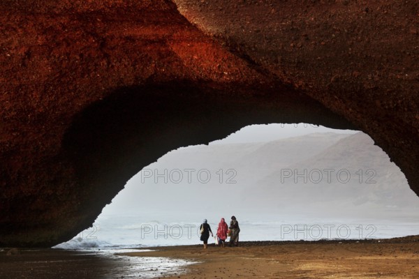 Impressive rock arch spanning the beach with silhouettes of visitors, Legzira, Souss-Massa region, Morocco