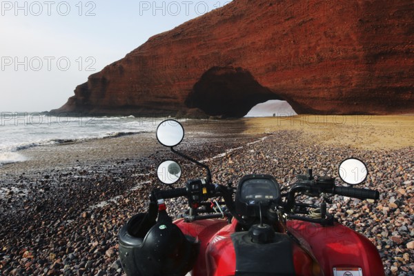 Quad bike on beach with impressive rock arch in Legzira, Legzira, Morocco