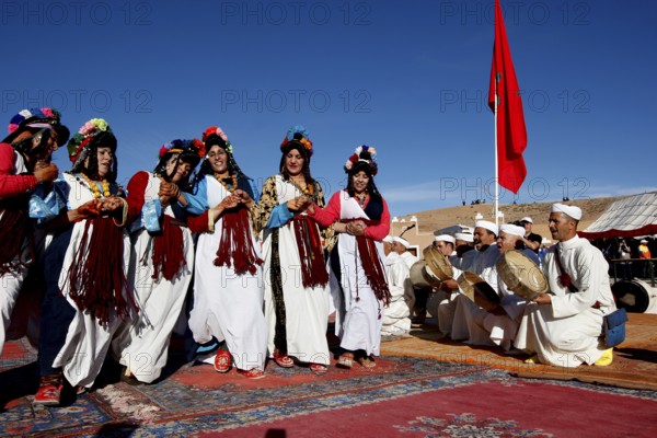 Women perform traditional Berber dance with an ensemble of musicians in the background under a blue sky, El Kelâa M'gouna