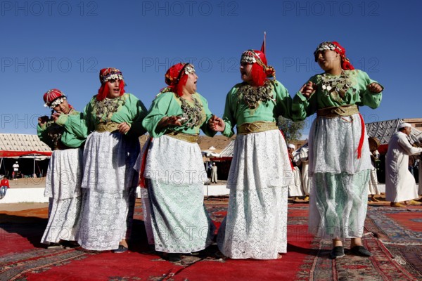 Dancing woman in traditional Berber clothes on colorful carpet during the Fête des Roses, El Kelâa m'Gouna