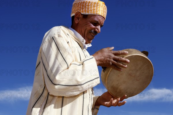 Smiling man playing drum during Fête des Roses in front of a clear sky, El Kelâa m'Gouna, Drâa-Tafilalet, Morocco