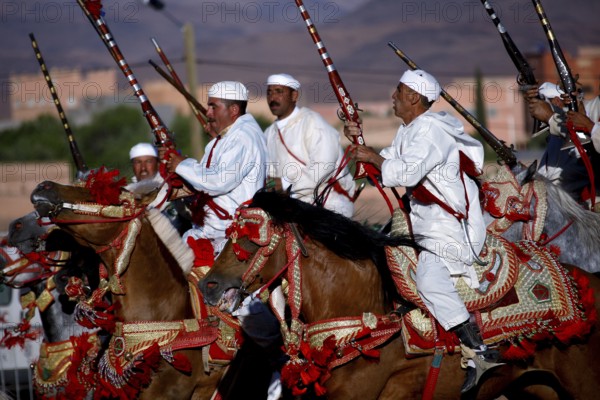 Fascinating parade of riders in white dress with magnificently decorated horses at a Fantasia, El Kelâa m'Gouna, Morocco