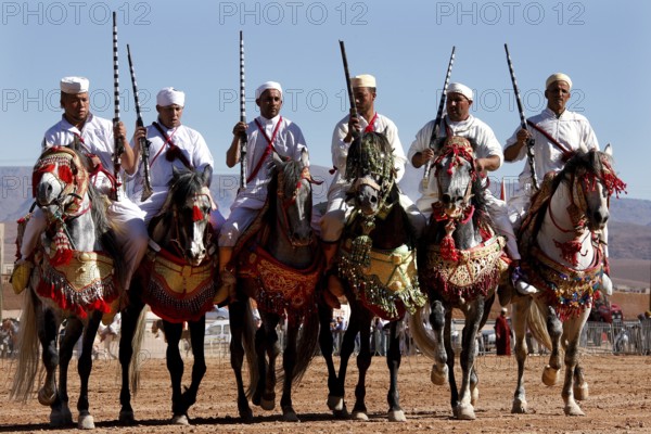 Six riders side by side on decorated horses at Fantasia, El Kelâa m'Gouna, Morocco