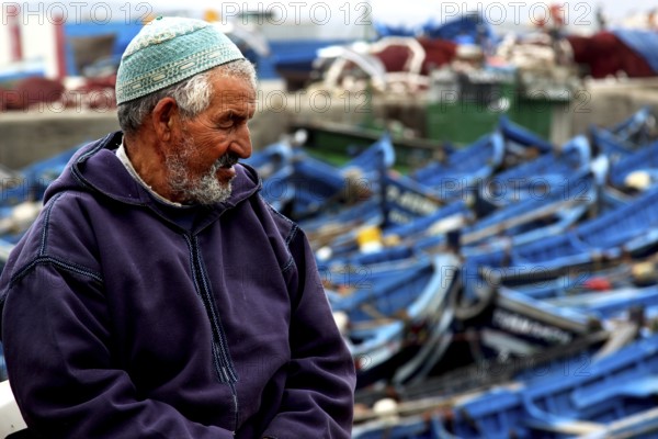 A fisherman sits in the harbor in front of numerous blue fishing boats, Essaouira, Marrakesh-Safi, Morocco