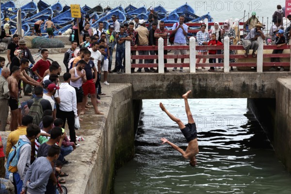 People gather at a bridge as a man jumps into water, Essaouira, Marrakesh-Safi, Morocco